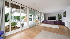 A spacious living area with large glass doors leading to a patio, a purple sofa, a flat-screen TV, and a potted plant.