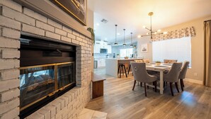 Eine moderne Küche mit Kochinsel, einem Essbereich mit Holztisch und Stühlen sowie einem Kamin mit Ziegelverkleidung.