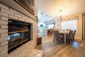 Eine moderne Küche mit Kochinsel, einem Essbereich mit Holztisch und Stühlen sowie einem Kamin mit Ziegelverkleidung.