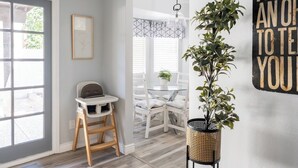Ein Zimmer mit Holzboden, Hochstuhl, Esstisch mit Stühlen, einer Pendelleuchte und einem an der Wand befestigten Schild.