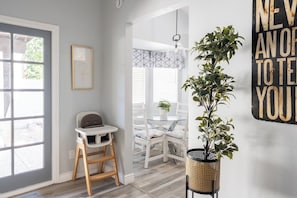 Ein Zimmer mit Holzboden, Hochstuhl, Esstisch mit Stühlen, einer Pendelleuchte und einem an der Wand befestigten Schild.