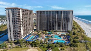 Ein Hochhaus-Hotel mit zahlreichen Balkonen, einem Poolbereich mit verschiedenen Pools und Blick auf den Strand.