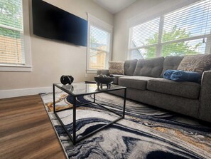 Ein modernes Wohnzimmer mit einer Couch, einem Glastisch und einem flachbildfernseher an der Wand.