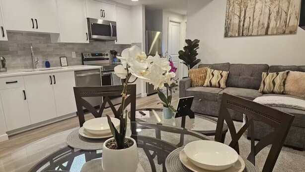 Una cocina moderna con armarios blancos, un microondas y un comedor con una mesa redonda y sillas.