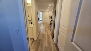 Un pasillo con suelo de madera, paredes blancas y puertas que dan a una zona de cocina.