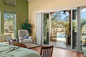 Ein Schlafzimmer mit Bett, Sessel, Tisch und einer Schiebetür, die auf eine Außenpatio mit Pool führt.