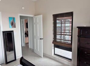 Ein Zimmer mit großem Fenster, einer Tür zu einem anderen Raum und einem Schminktisch.