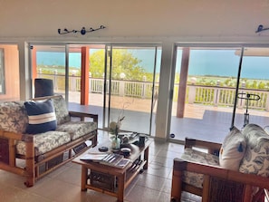 A room with a sofa, a small table, and a view of a balcony with a railing and trees. - The Serene Getaway  - Chic Private Room & Bath Near Grace Bay (Providenciales)