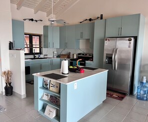 Eine moderne Küche mit hellblauen Schränken, einer zentralen Kochinsel, einem Edelstahlkühlschrank und einem eingebauten Backofen.