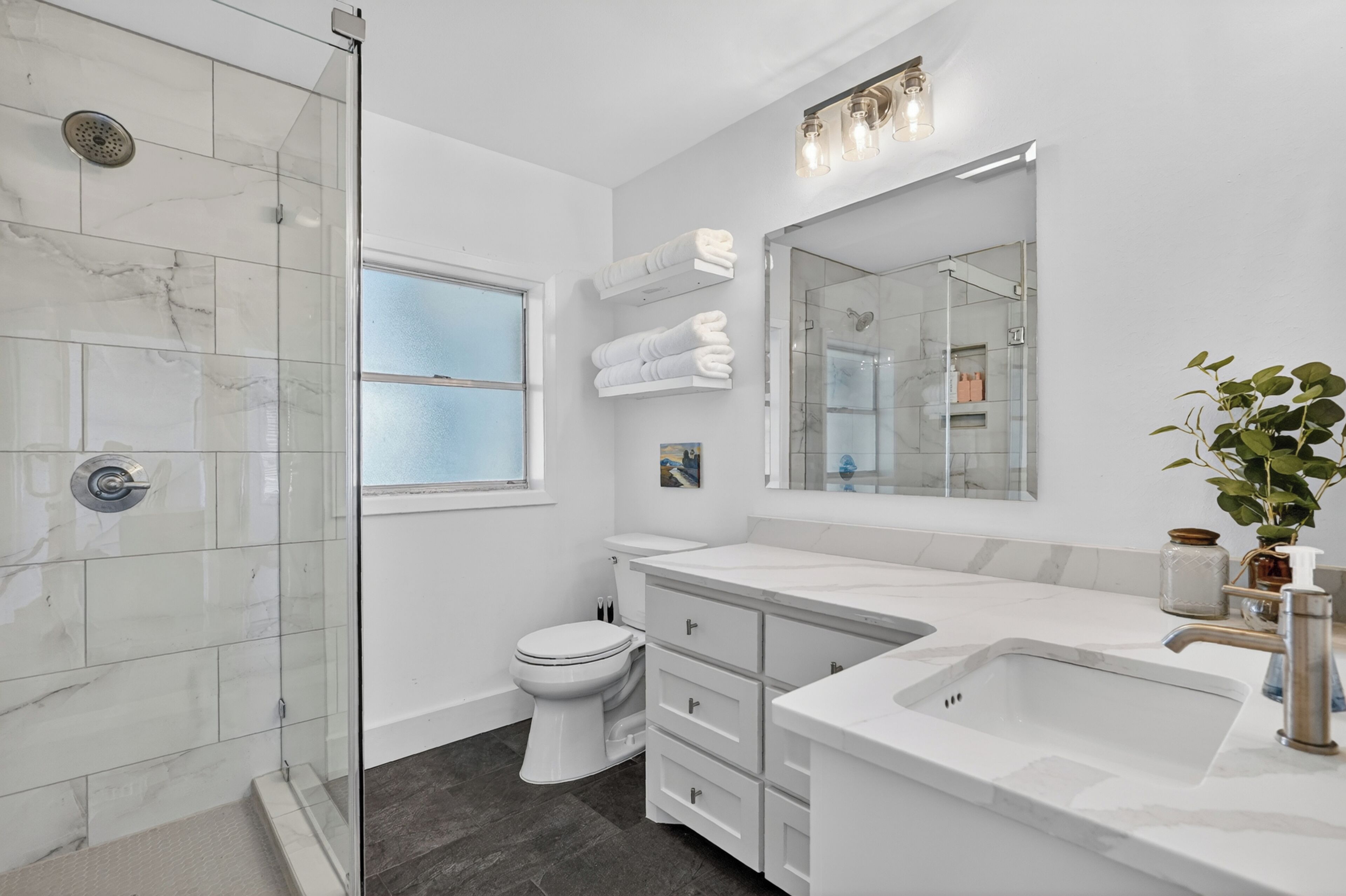 Un baño moderno con cabina de ducha de vidrio, inodoro, lavamanos y un espejo grande.