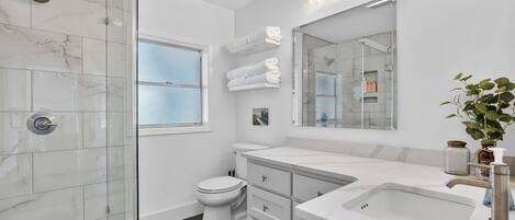 Un baño moderno con cabina de ducha de vidrio, inodoro, lavamanos y un espejo grande.