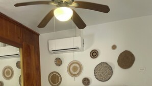 A bedroom with a wooden headboard, a ceiling fan, an air conditioning unit, and decorative wall hangings. - Your tropical escape in Playa Santa, Guanica. Beach days starts here. (Guánica)