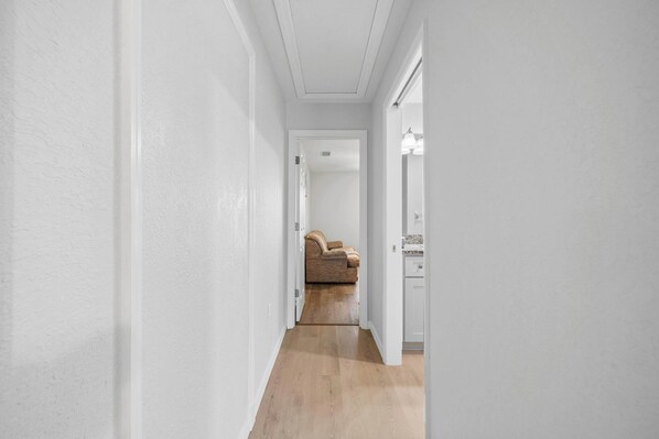A narrow hallway with wooden flooring and white walls, leading to a room with a brown leather sofa. - Private 1-Bedroom with Private Entrance Ocala, FL (Ocala)