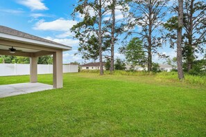 A covered patio area with a concrete floor, surrounded by a grassy yard and tall pine trees. - Private 1-Bedroom with Private Entrance Ocala, FL (Ocala)