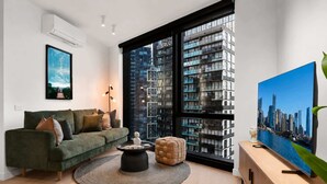 Ein modernes Wohnzimmer mit einem grünen Sofa, einem runden Couchtisch und einem großen Fenster mit Blick auf die Stadt.