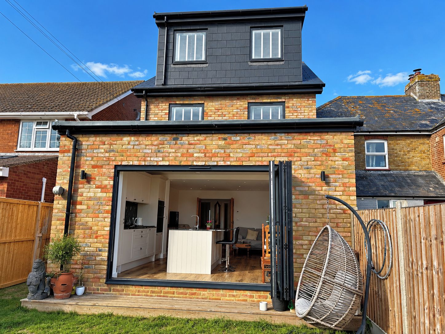 A two-story house with a large open-plan kitchen and dining area, a separate living room, and a small outdoor seating area.