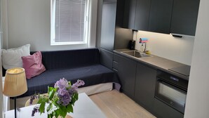 Un espacio habitable pequeño con kitchenette, un sofá, una lámpara y una ventana con persianas.