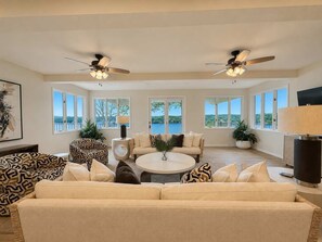 A spacious living room with a large sofa, a coffee table, and two ceiling fans. - Cliff Top Retreat Spacious (Sunrise Beach)