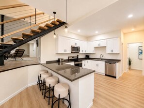 A modern kitchen with a central island, stainless steel appliances, and a wooden staircase. - Cliff Top Retreat Spacious (Sunrise Beach)