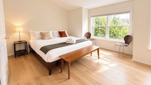 A bedroom with a bed, bedside tables, a bench, a chair, and a large window with a view. - Central Ballard Townhome / Sleeps 8 / Direct Bus Line to Stadium (Seattle)
