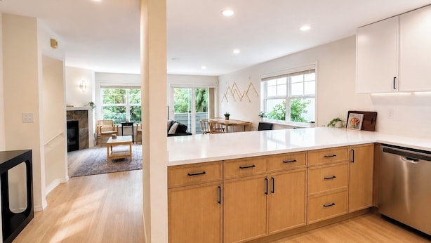 A modern kitchen with wooden cabinets, a stainless steel dishwasher, and a large window providing natural light. - Central Ballard Townhome / Sleeps 8 / Direct Bus Line to Stadium (Seattle)