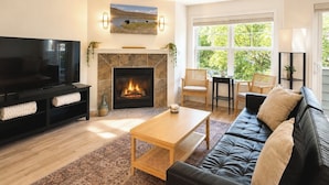 A living room with a fireplace, a television, a sofa, and a large window. - Central Ballard Townhome / Sleeps 8 / Direct Bus Line to Stadium (Seattle)