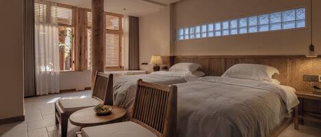 Quarto de hotel com duas camas, uma mesinha com uma cesta de frutas e uma cadeira.