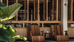Un espace extérieur aménagé avec des meubles en bois, comprenant des chaises et des tables, un pot de fleurs et un mur avec des lattes verticales.