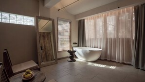 Une salle de bain moderne avec une baignoire sur pieds, une chaise en bois sur laquelle est posé un panier de fruits, et un miroir.