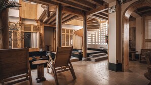 Un intérieur en bois avec un plafond haut, des poutres apparentes et un espace salon comprenant une table ronde et des chaises.