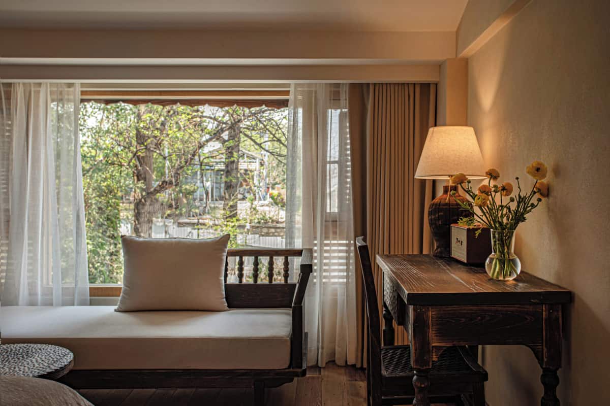 A room with a bed, a table with a lamp, and a vase with flowers.