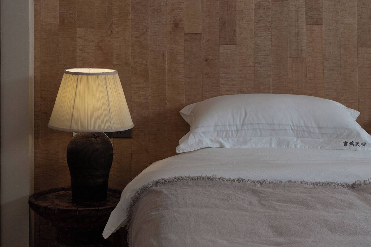 A bedroom with a wooden headboard, a bedside lamp, a bed with white bedding, and a small wooden nightstand.