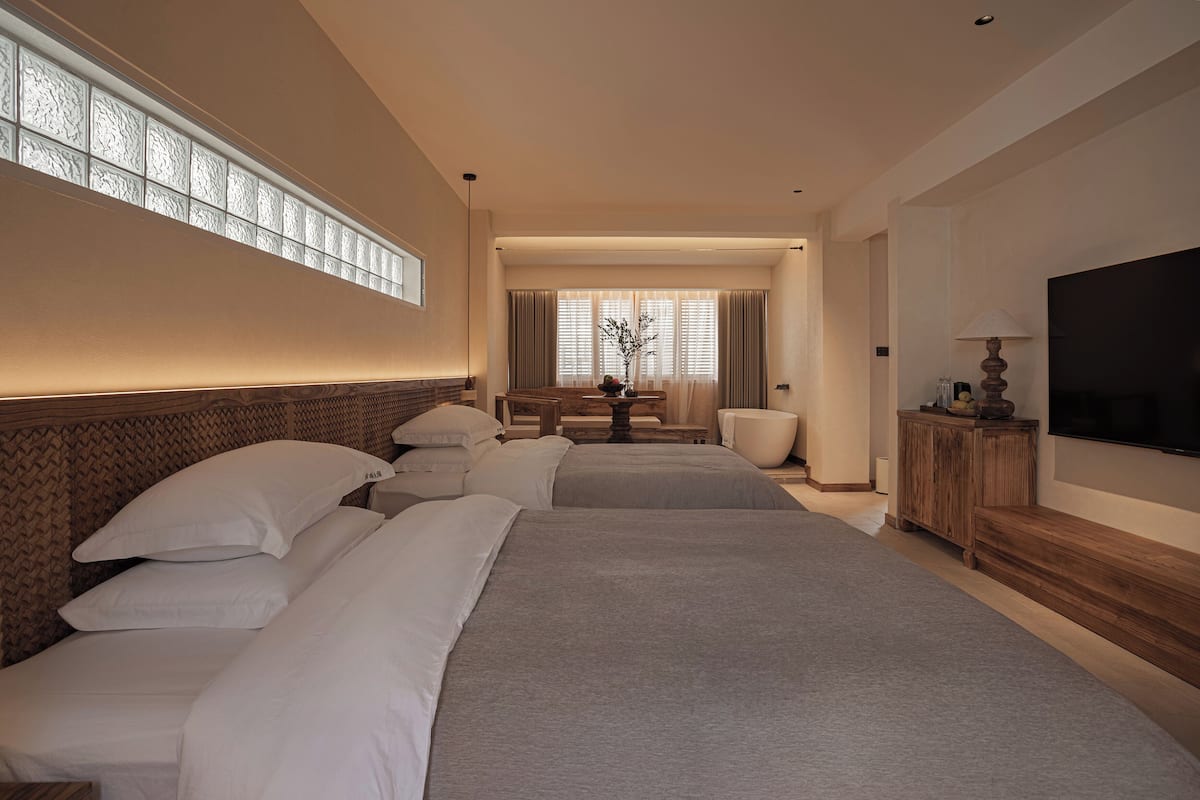 A hotel room with a large bed, a TV, a wooden cabinet, and a window with curtains.