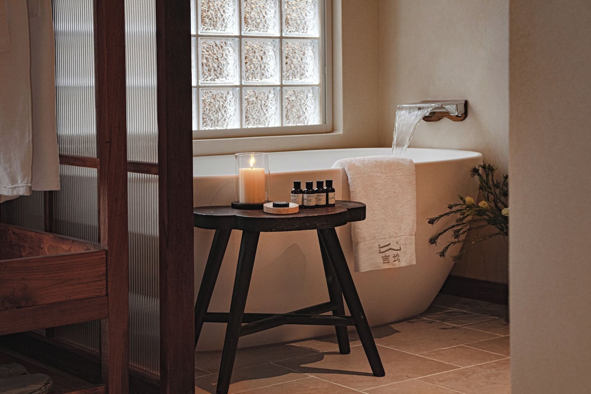A bathroom with a bathtub, a window with frosted glass, a candle, and a small table with toiletries.