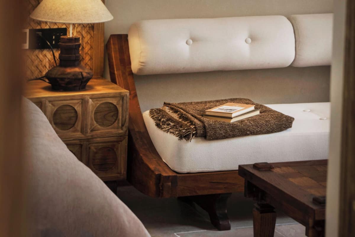 A room with a cushioned bench, a lamp, and a small table with a book.