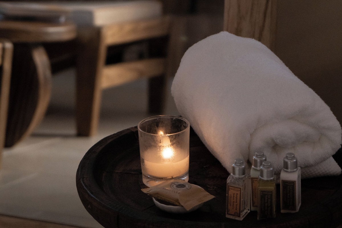 A candle on a wooden table with a white towel and essential oils.