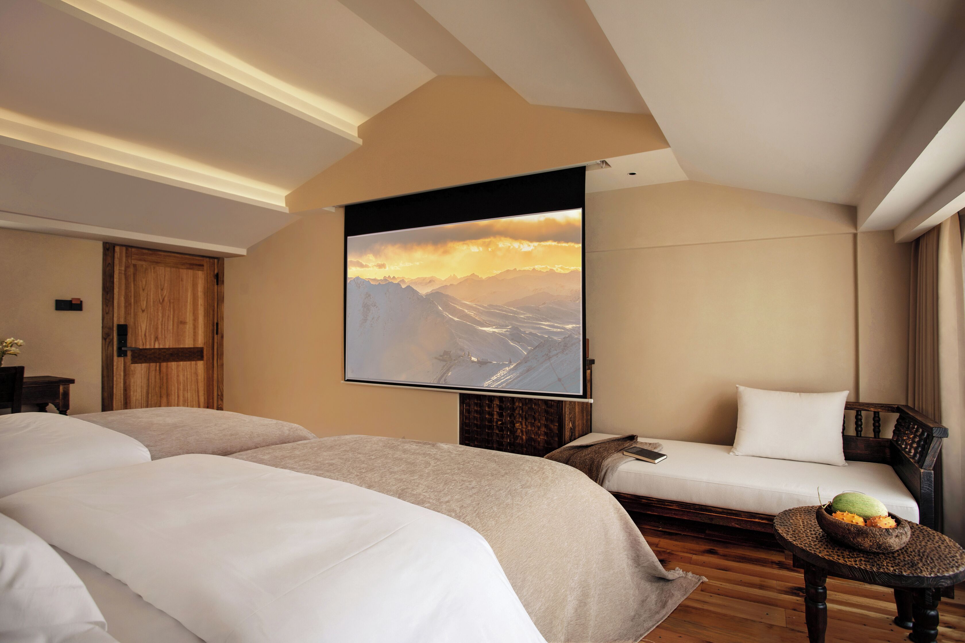 A hotel room with two beds, a sofa, a television, and a small table with fruit.
