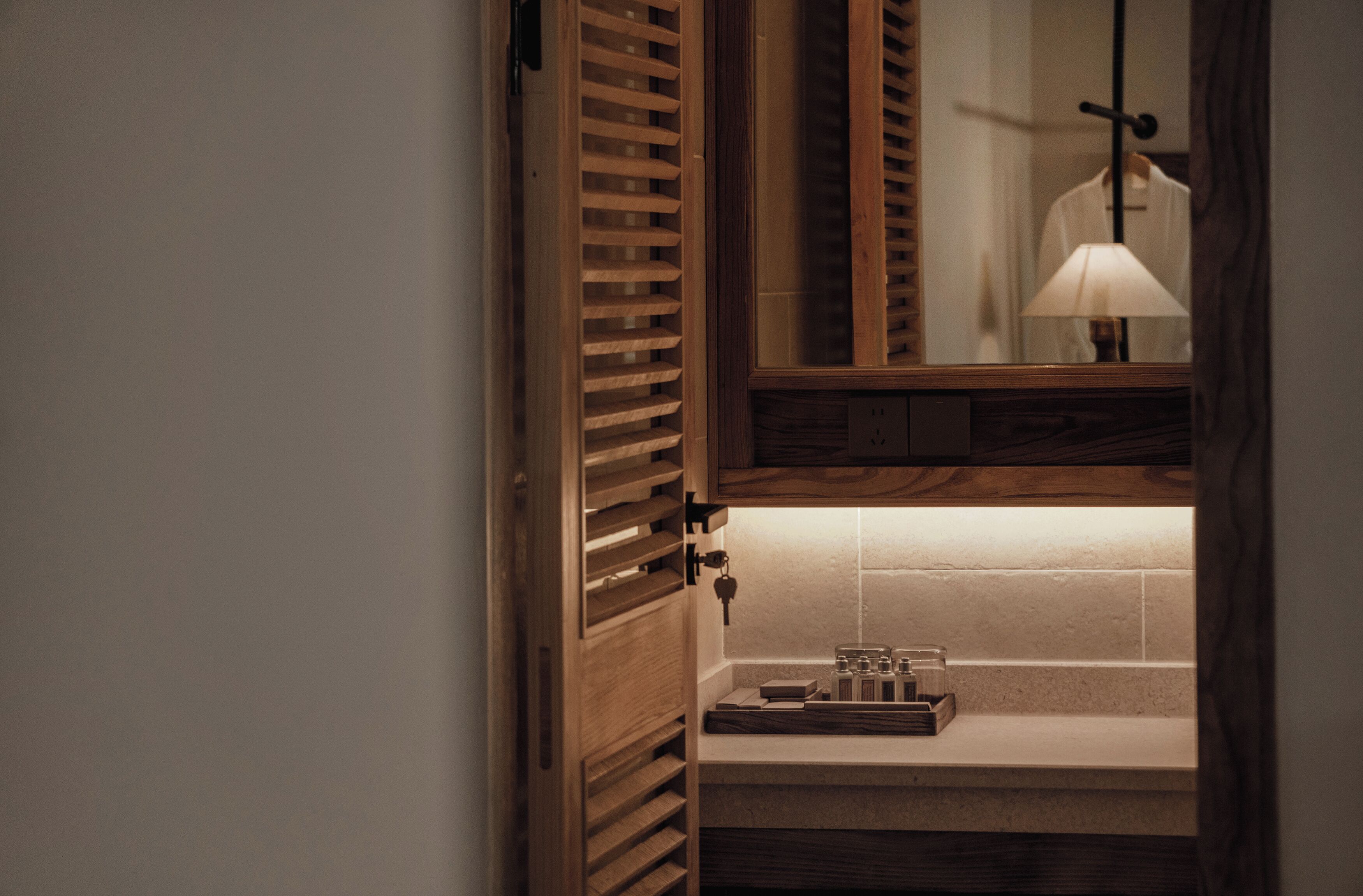 Un meuble en bois avec un miroir, une lampe suspendue et un plateau avec des bouteilles.