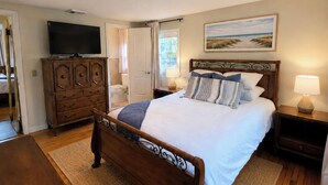 Une chambre à coucher avec un lit en bois, un téléviseur posé sur une commode et un tableau accroché au mur.