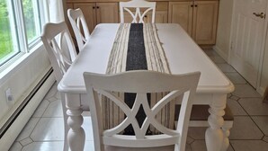 Un coin repas avec une table blanche, des chaises, un lustre et des meubles de rangement en bois.