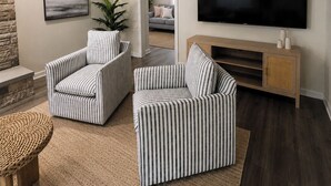 Un salon avec des fauteuils à rayures, un téléviseur à écran plat, une cheminée en pierre et un tapis tissé.