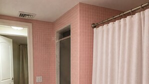 Une salle de bain avec des murs recouverts de carreaux roses, une douche avec une porte en verre et un rideau de douche blanc.