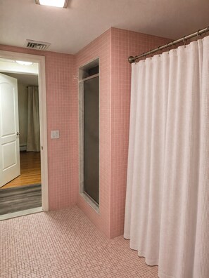 Ein Badezimmer mit rosa gefliesten Wänden, einer Dusche mit Glastür und einem weißen Duschvorhang.