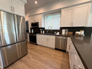 A modern kitchen with stainless steel appliances, white cabinetry, and a window with blinds. - {SURF INN} Pacific Beach-La Jolla area Beach Haus with Modern Designer Vibes (San Diego)
