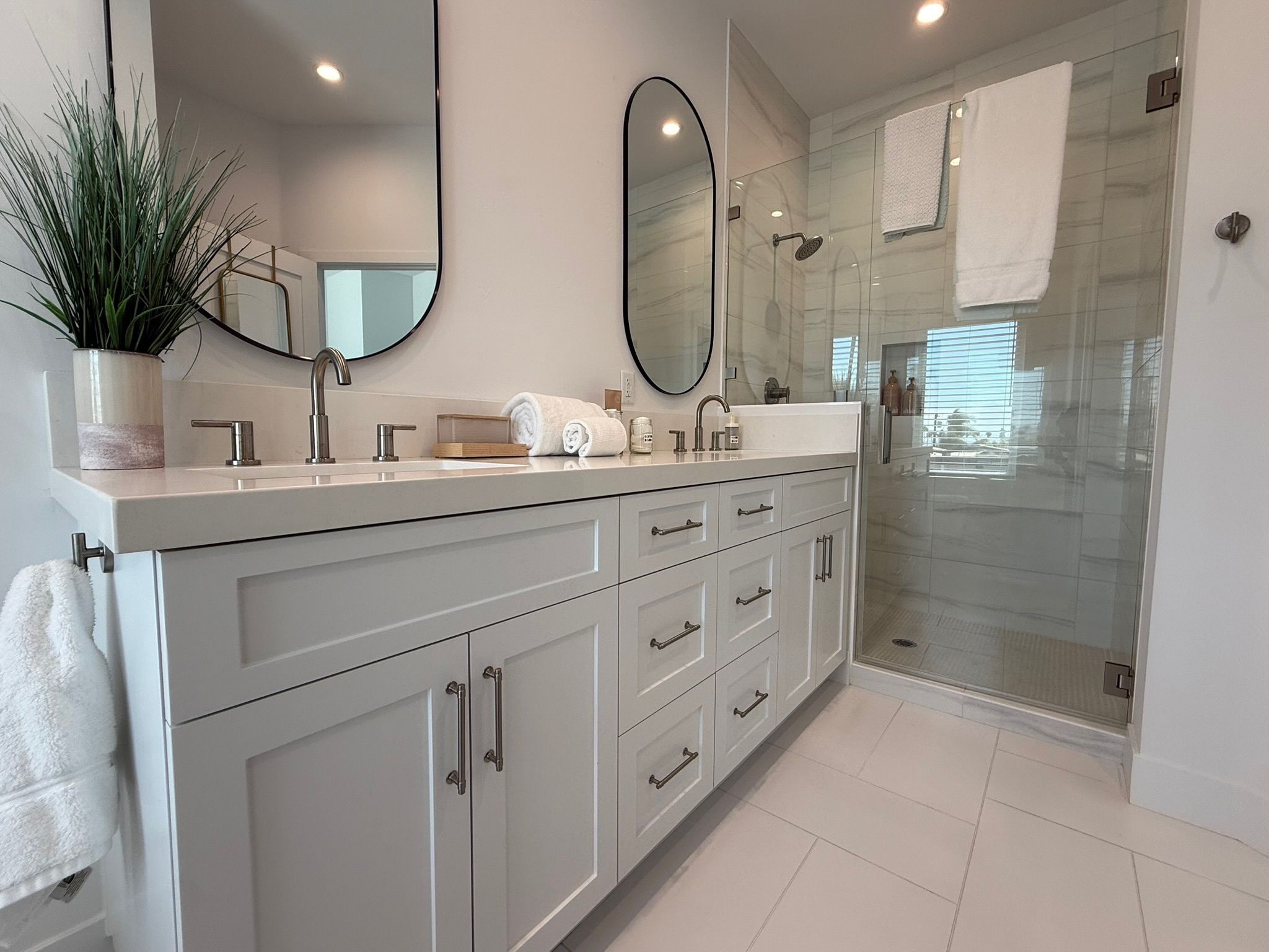 A modern bathroom with a glass shower enclosure, a large mirror, and a potted plant.