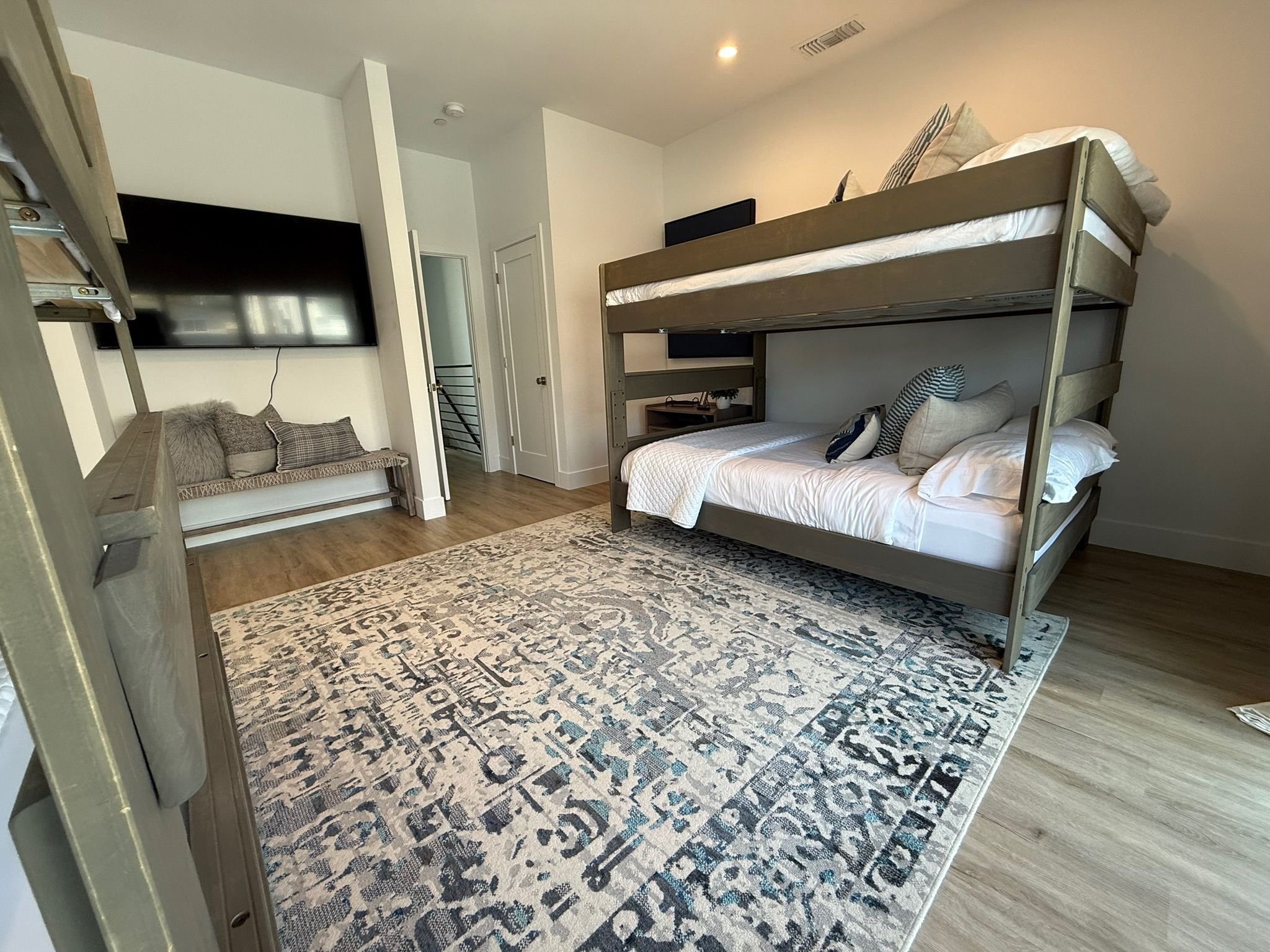 A bunk bed with a patterned rug, a sofa with cushions, and a TV mounted on the wall.