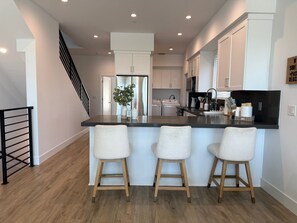 A modern kitchen with a central island, bar stools, and a staircase. - {SURF INN} Pacific Beach-La Jolla area Beach Haus with Modern Designer Vibes (San Diego)