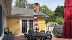 Een geel huis met schoorsteen, een terras met tafel en stoelen, en een rode parasol.