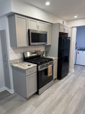 A modern kitchen with grey cabinetry, a stainless steel stove, a microwave, and a black refrigerator. - Perfect 3-bedroom house with AC in beautiful Parma Heights (Parma Heights)