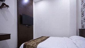 A hotel room with a bed, a TV mounted on the wall, a small trash bin, and a wooden panel. - Islander Lodge by LWE (George Town)